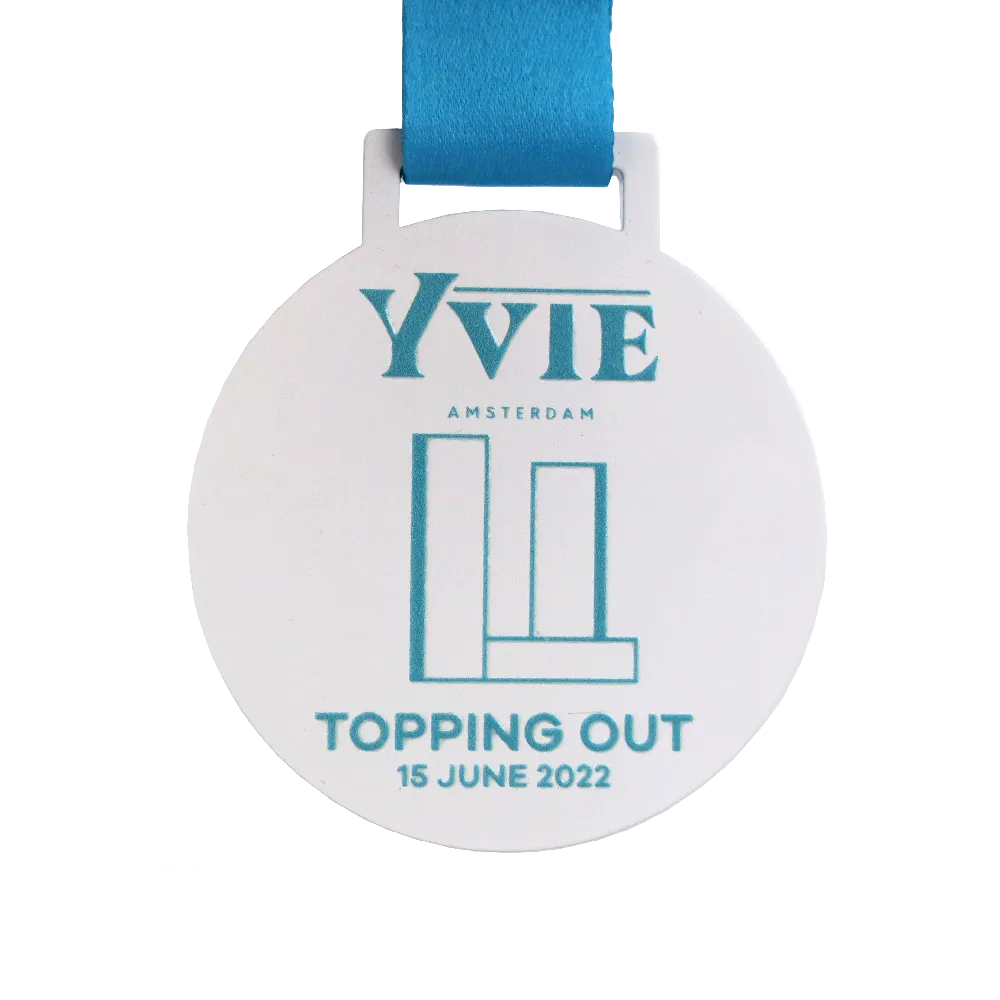 YVIE Amsterdam Richtfest. Weiße runde Medaille mit blauer Beschriftung